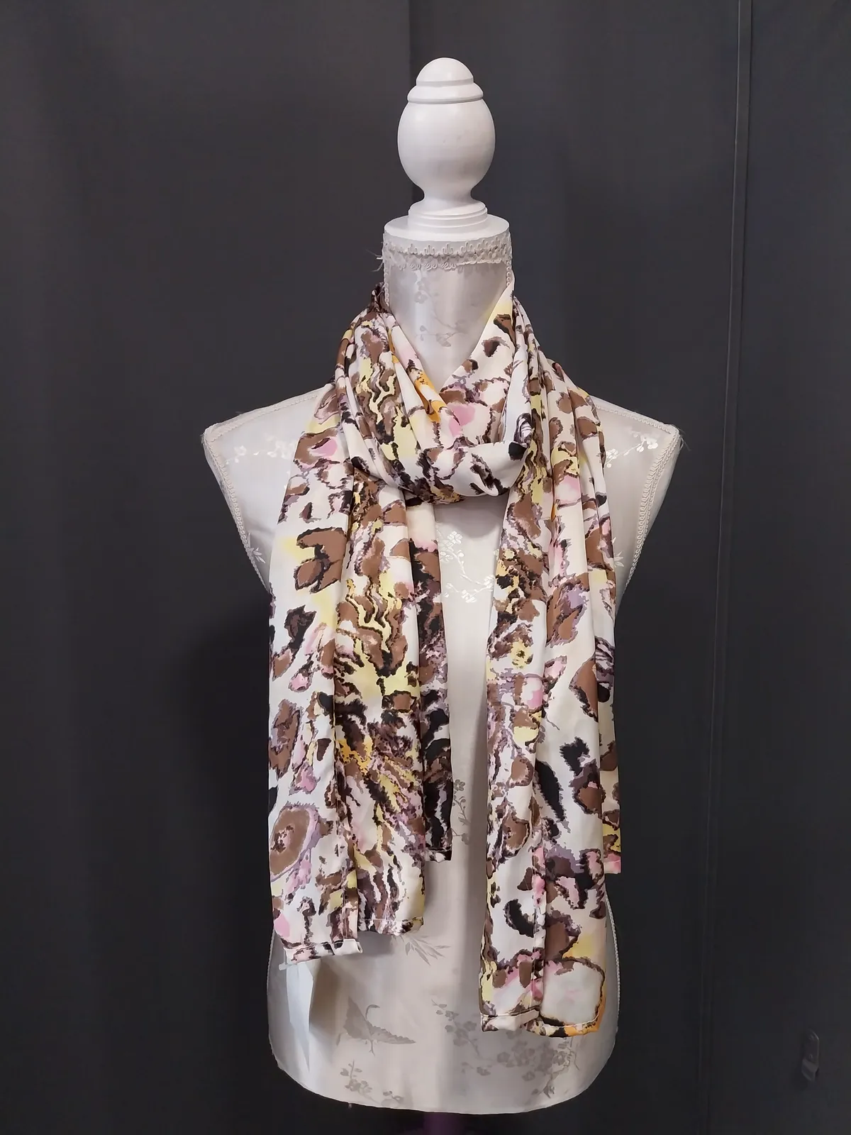 Foulard blanc imprimé de motifs floraux taupe, roses et jaunes, noué autour du cou d'un buste mannequin