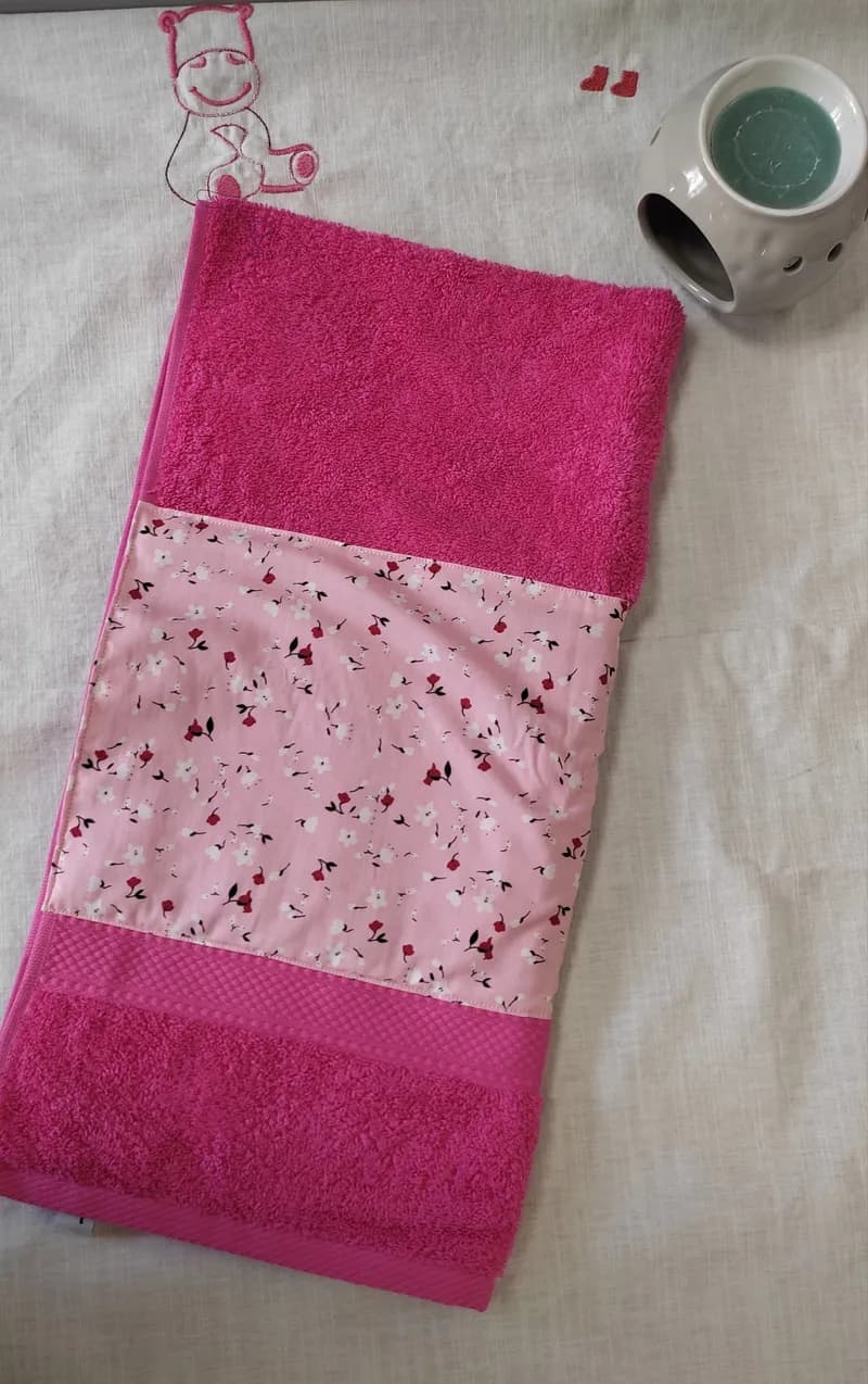 Serviette éponge fuchsia pliée, bande brodée de petites fleurs roses et blanches sur fond rose pâle