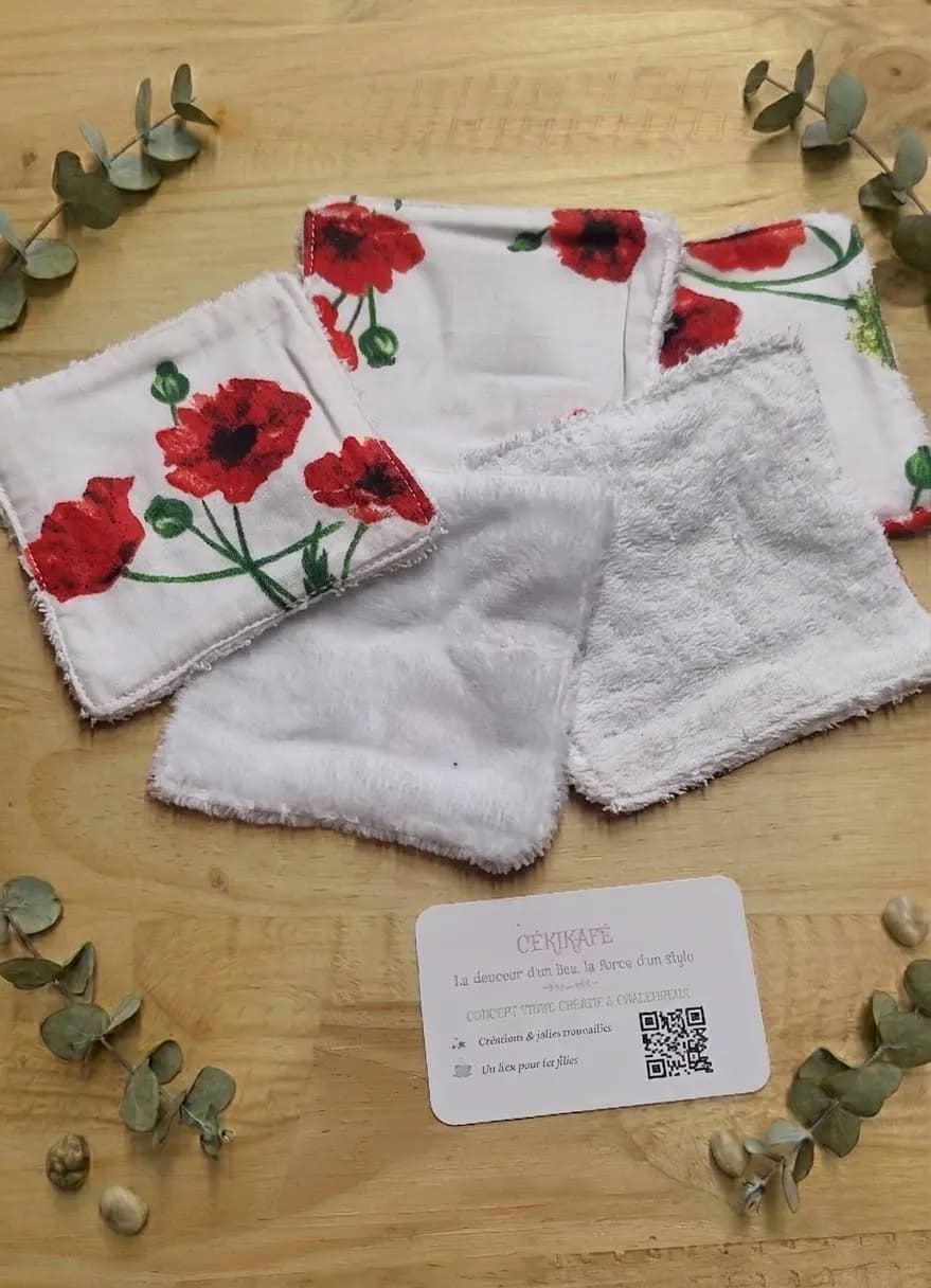 Quatre lingettes démaquillantes lavables, deux imprimées coquelicots rouges et deux en éponge blanche, posées sur du bois avec des branches d'eucalyptus séché