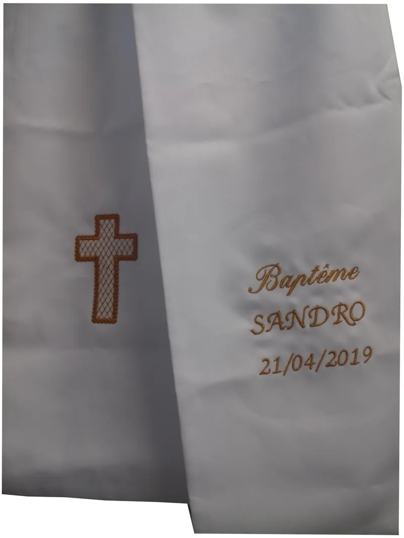 Écharpe de baptême blanche drapée, brodée sur un pan d'une croix pleine dorée au contour épais et à l'intérieur en motif quadrillé, et sur l'autre pan du mot « Baptême », du prénom SANDRO et de la date 21/04/2019 en fil doré, exemple de réalisation avec un autre prénom que celui choisi à la commande
