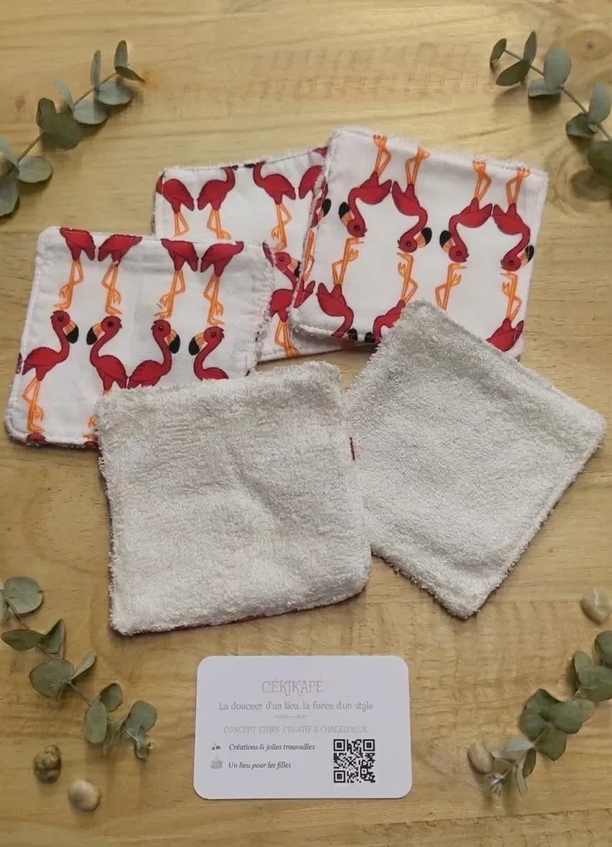 Cinq lingettes lavables carrées posées sur une table en bois. Trois montrent la face en coton blanc imprimé de flamants rouges aux pattes orange. Deux montrent l'autre face, en éponge de bambou blanc cassé. Autour, des brins d'eucalyptus, des galets et une carte de visite CÉKIKAFÉ.