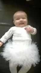 Bébé souriant vêtu d'un body blanc à manches longues et d'une jupe tutu en tulle blanc très gonflante, avec des collants blancs