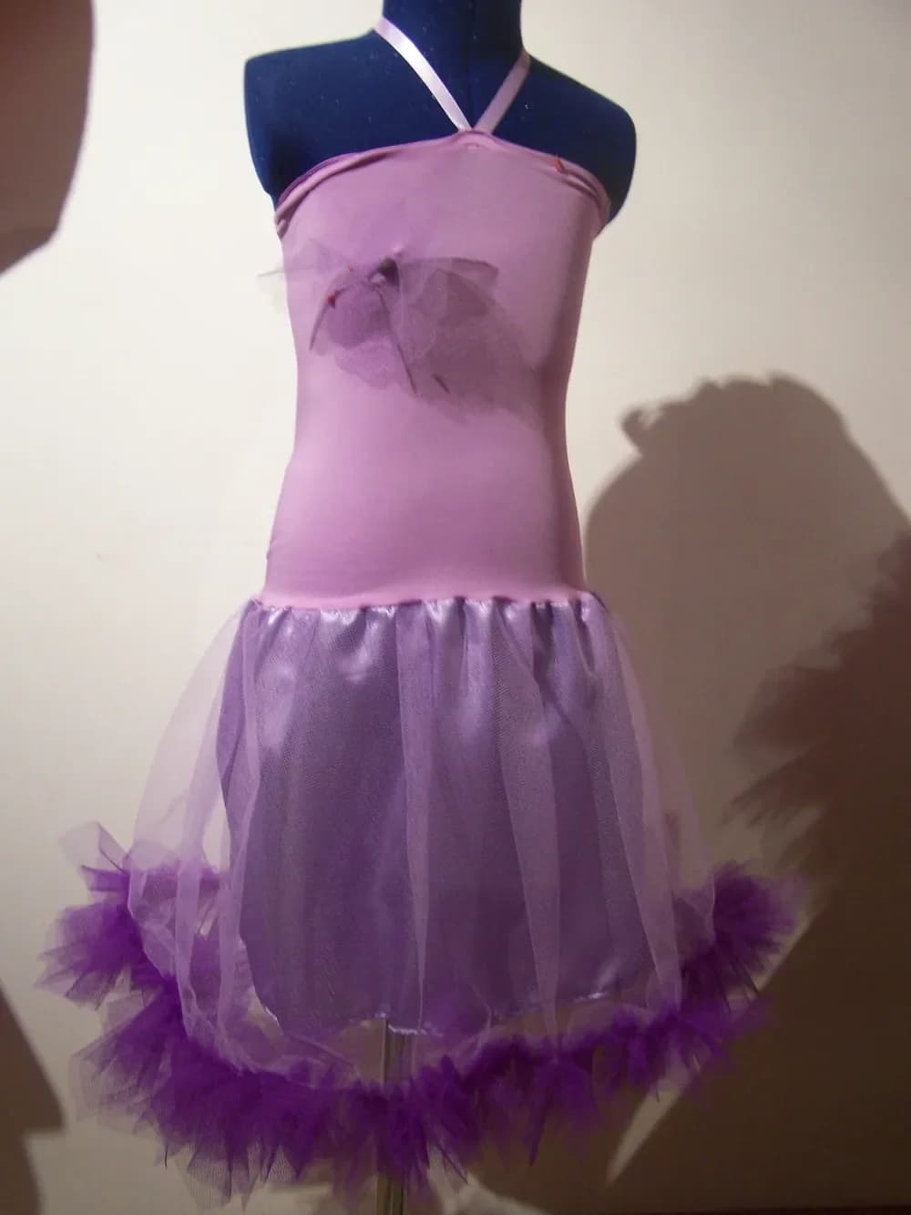 Robe sur un buste de couture : haut en jersey lilas à bretelles nouées autour du cou, petite fleur en tulle sur le devant, et longue jupe en tulle lilas transparent bordée en bas d'un volant de tulle violet