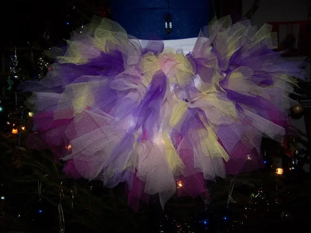 Jupe tutu très bouffante sur un buste, devant un sapin de Noël illuminé, en tulle violet, jaune pâle et blanc mêlés