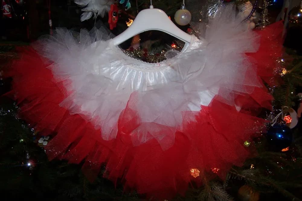 Jupe tutu sur un cintre blanc devant un sapin de Noël, avec un volant de tulle blanc en haut et de grands volants de tulle rouge en dessous