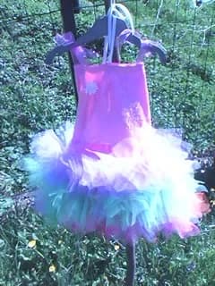 Robe tutu suspendue à un cintre noir dans un jardin : haut rose fuchsia orné d'une fleur et jupe en tulle blanc, rose, bleu et violet