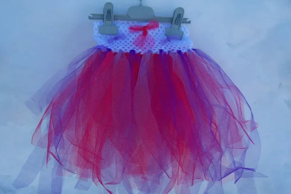 Petite robe tutu sur un cintre : haut en dentelle crochet blanche orné d'un nœud rouge et jupe en longues bandes de tulle rouge et violet