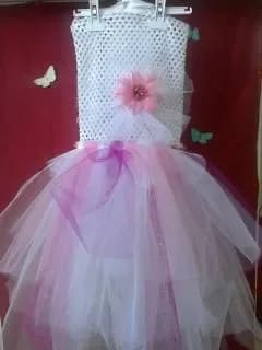 Robe sur un cintre : haut en dentelle crochet blanche orné d'une fleur rose et longue jupe en tulle blanc et rose pâle, avec des rubans violets