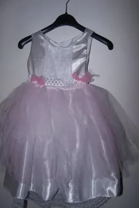Robe sur un cintre noir : corsage en satin blanc, ceinture de dentelle blanche ornée de fleurs roses et jupe en tulle rose pâle sur un jupon de satin blanc