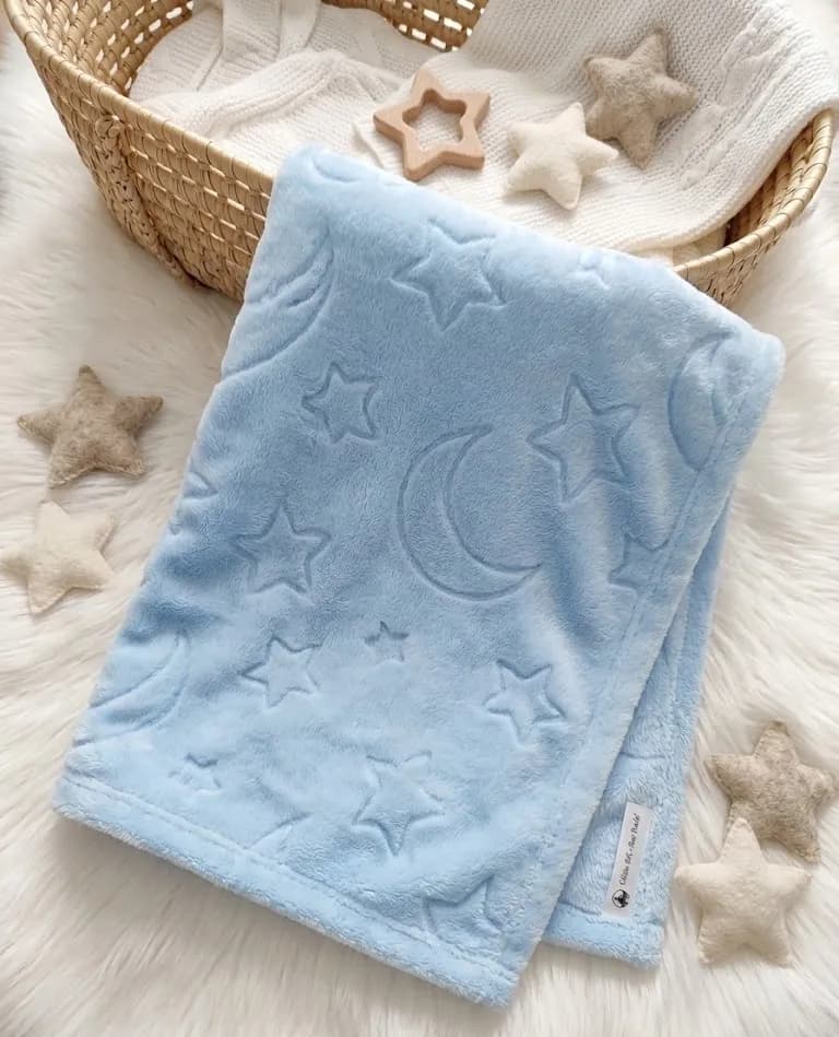 Couverture polaire bleue à motifs lune et étoiles, pliée dans un panier en osier avec des étoiles en tissu