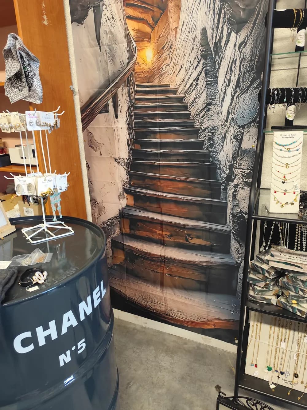 Décor mural en trompe-l'œil représentant un escalier en pierre, entouré de présentoirs à bijoux et colliers dans la boutique