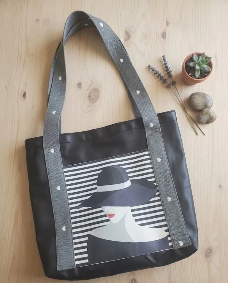 Sac cabas noir avec anses grises à clous en forme de cœur et illustration d'une femme au chapeau