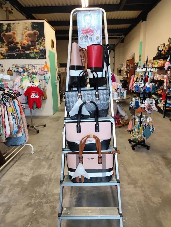 Sacs à main présentés sur une échelle en escabeau, avec vêtements et peluches pour bébé en arrière-plan