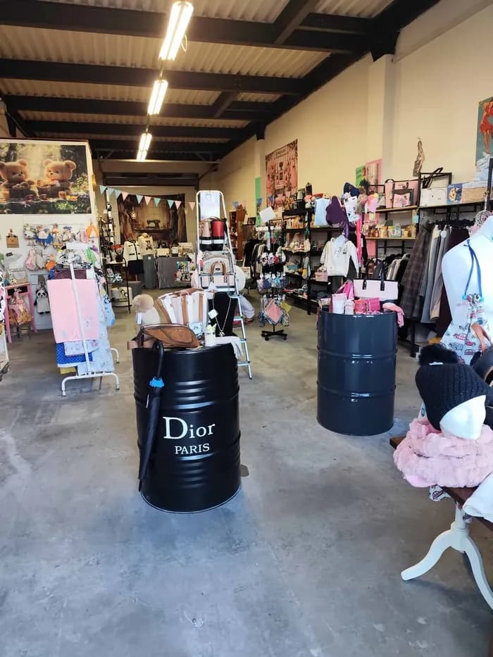 Allée de la boutique avec deux présentoirs en tonneau noir « Dior Paris », entourés de vêtements et sacs