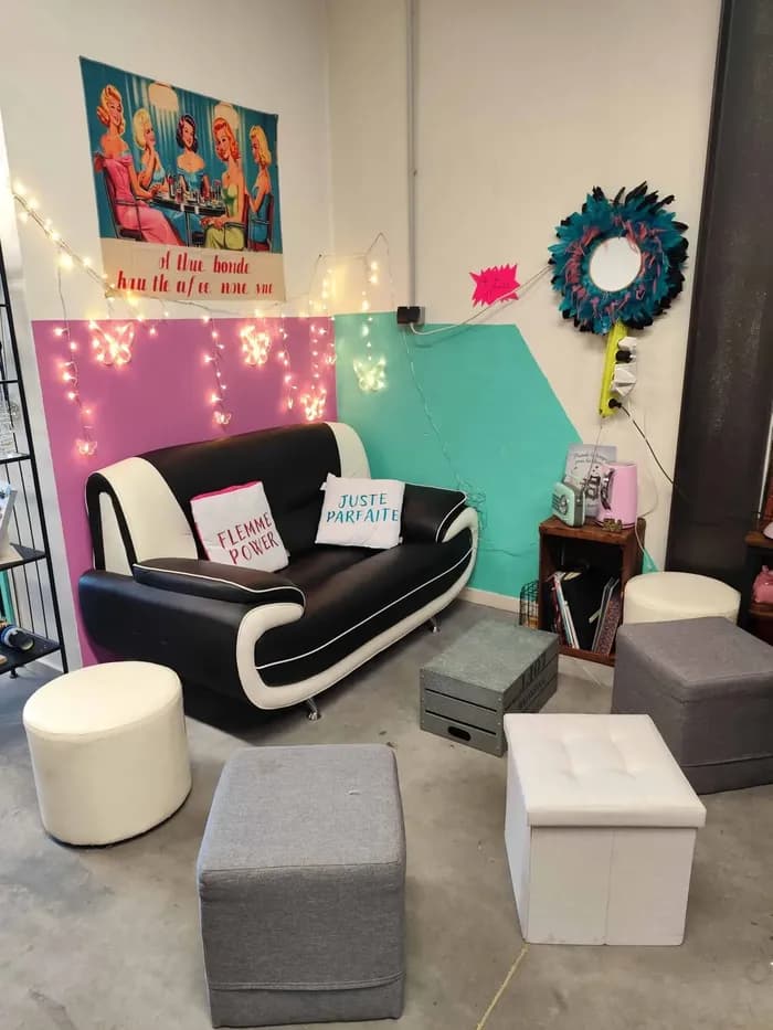 Coin salon cosy de la boutique avec canapé noir et blanc, coussins brodés « Flemme Power » et « Juste Parfaite », guirlande lumineuse
