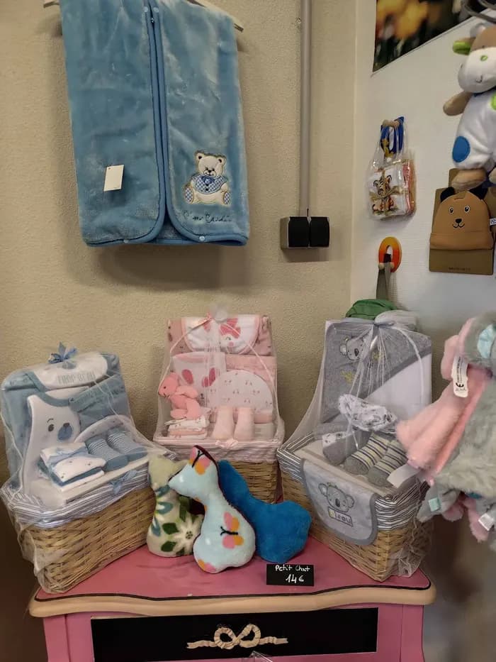 Étagère avec paniers-cadeaux de naissance et gigoteuse bleue brodée d'un ourson, sur un meuble rose