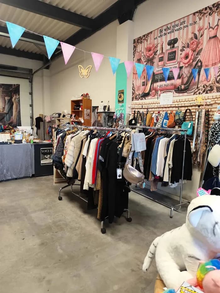 Portants de vêtements femme vintage sous une fresque « Be who you are », près d'une enseigne Vogue