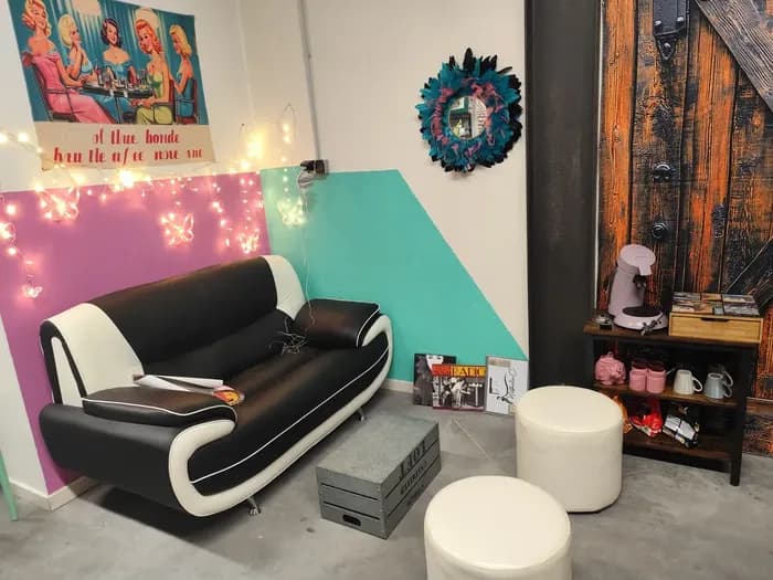 Coin salon rétro de la boutique avec canapé noir et blanc, miroir à plumes bleues et petite étagère bar rose