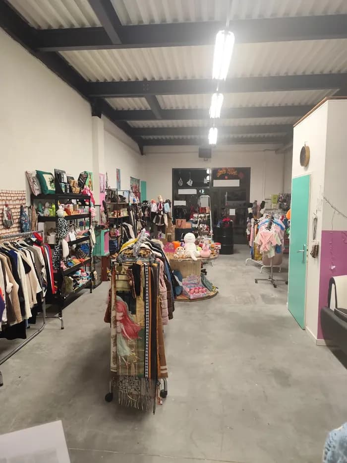 Allée de la boutique avec portants de vêtements, tourniquet à écharpes et présentoirs de peluches
