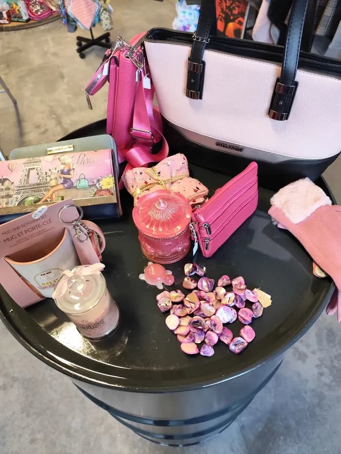 Assortiment de sacs et accessoires roses — sac à main, portefeuille, porte-clés et bijoux — sur un tonneau noir