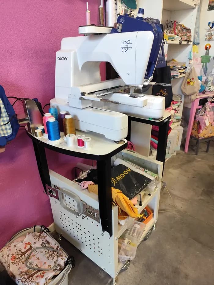 Machine à broder Brother sur son meuble, entourée de bobines de fil colorées et d'accessoires bébé