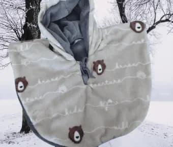 Cape bébé réversible capuche relevée, face en polaire gris clair ornée de visages d'ours marron et de mots manuscrits blancs, capuche doublée de polaire grise unie et lien gris au cou, présentée devant une forêt enneigée