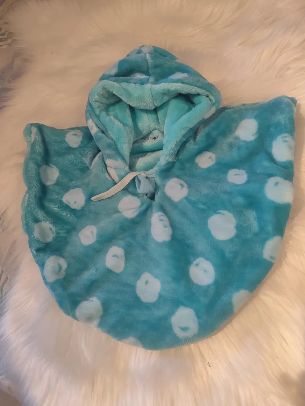 Cape bébé réversible Pomme verte CÉKIKAFÉ posée sur une fourrure blanche, capuche relevée, face en douillette épaisse vert d'eau turquoise semée de ronds blancs en forme de petites pommes, capuche doublée de vert d'eau uni et lien blanc noué au cou.