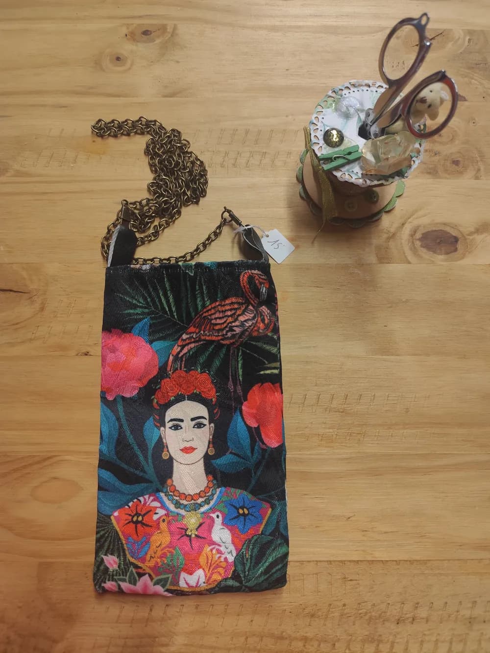 Sac pochette téléphone en tissu imprimé du portrait de Frida Kahlo entourée de fleurs tropicales roses et d'un flamant rose, chaîne dorée en bandoulière, étiquette encore accrochée